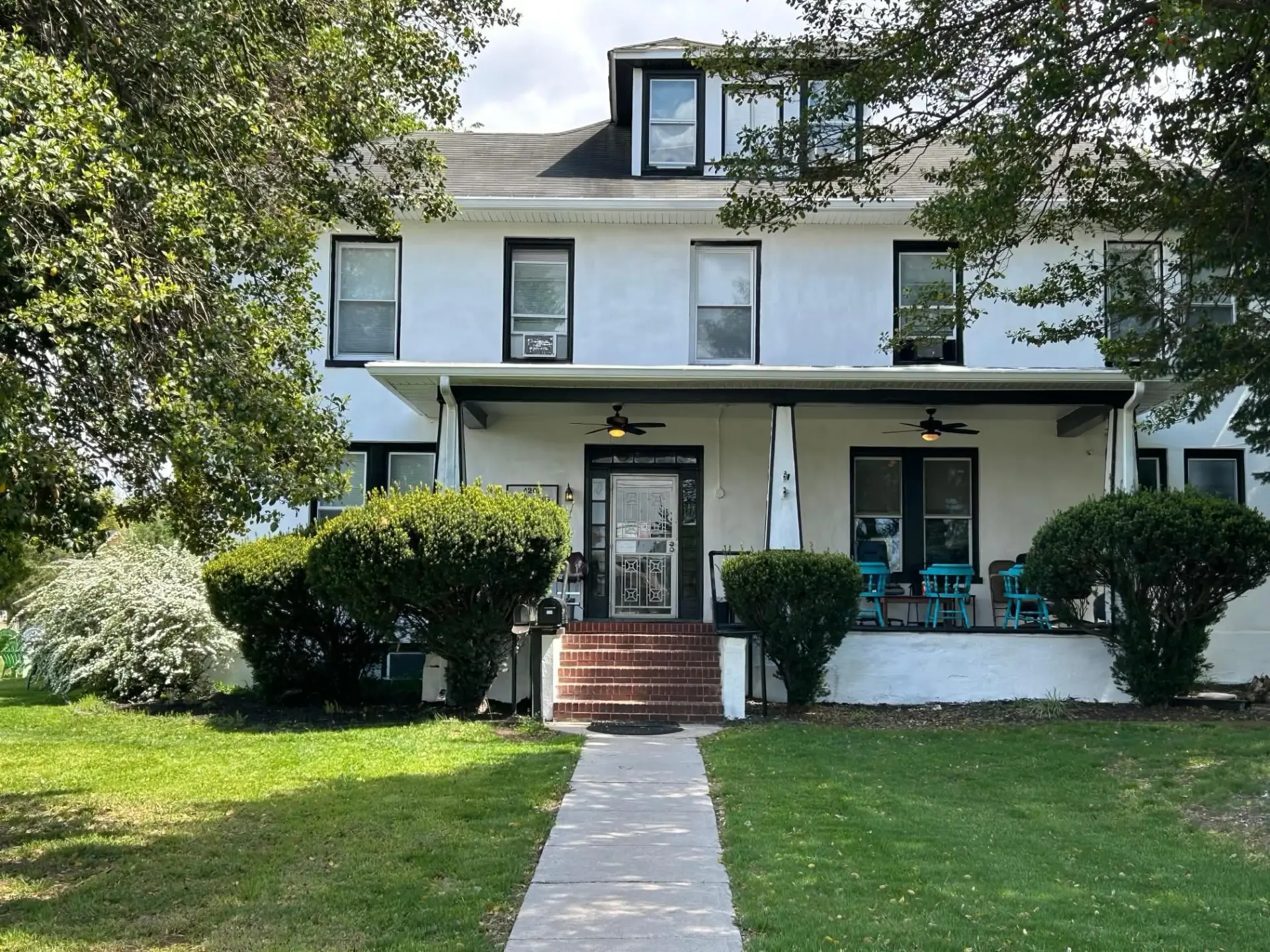 The front of a Damascus House residence with a covered porch, shade trees, and a front lawn